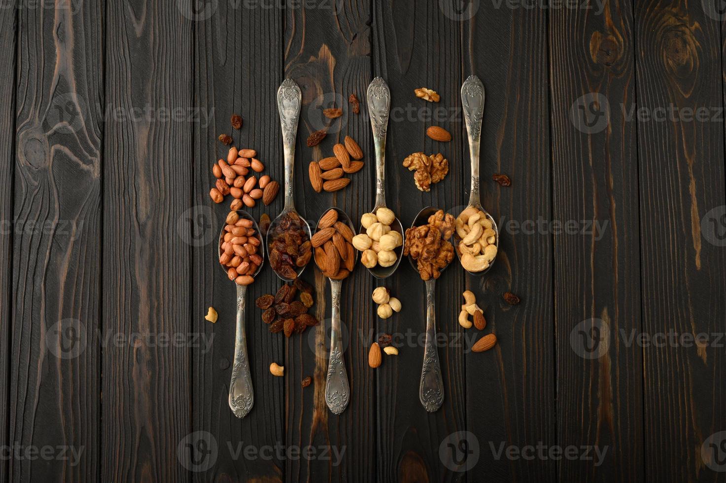 Hazelnut, cashews, raisins, almonds, peanuts, walnuts in silver spoons on a rustic background photo