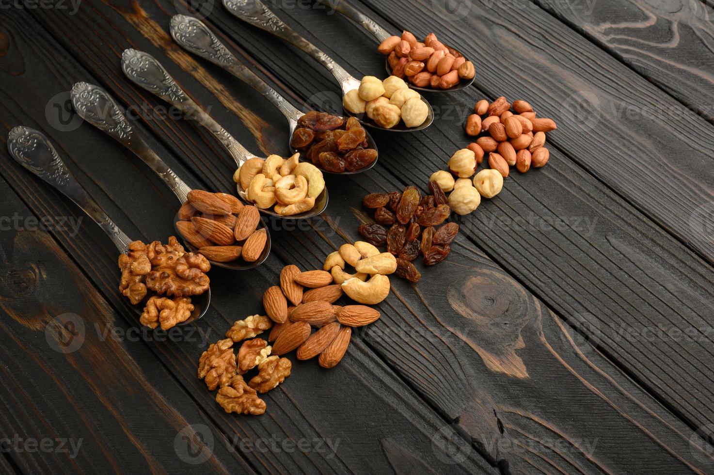 avellanas, anacardos, pasas, almendras, cacahuetes, nueces en cucharas de plata sobre un fondo rústico foto