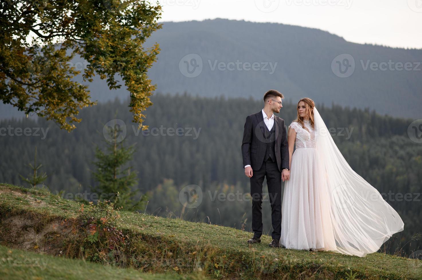 happy stylish bride and groom running and having fun in mountains on summer sunny day photo