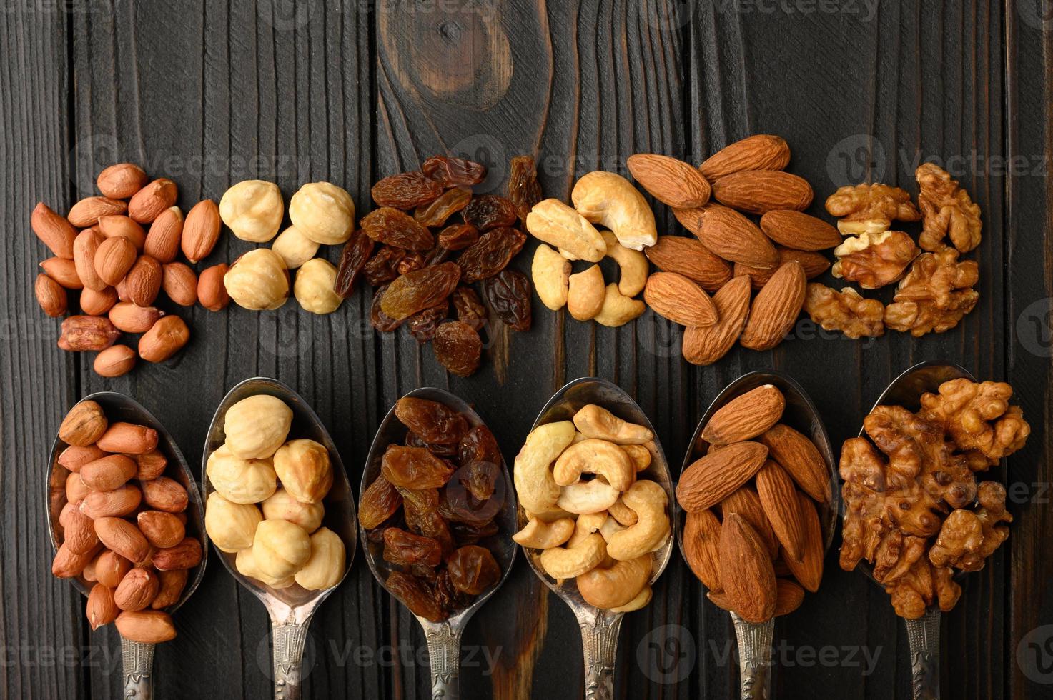 Hazelnut, cashews, raisins, almonds, peanuts, walnuts in silver spoons on a rustic background photo