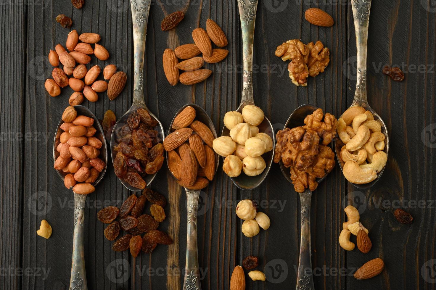 avellanas, anacardos, pasas, almendras, cacahuetes, nueces en cucharas de plata sobre un fondo rústico foto