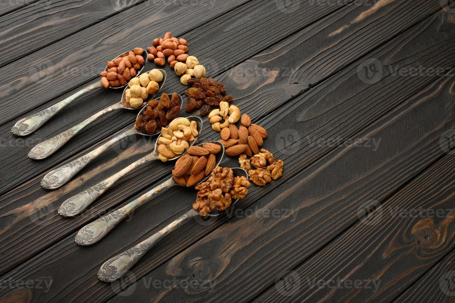 avellanas, anacardos, pasas, almendras, cacahuetes, nueces en cucharas de plata sobre un fondo rústico foto