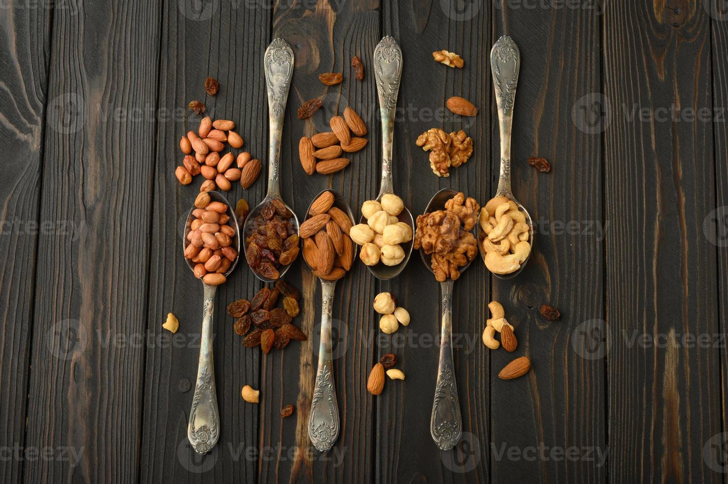 avellanas, anacardos, pasas, almendras, cacahuetes, nueces en cucharas de plata sobre un fondo rústico foto