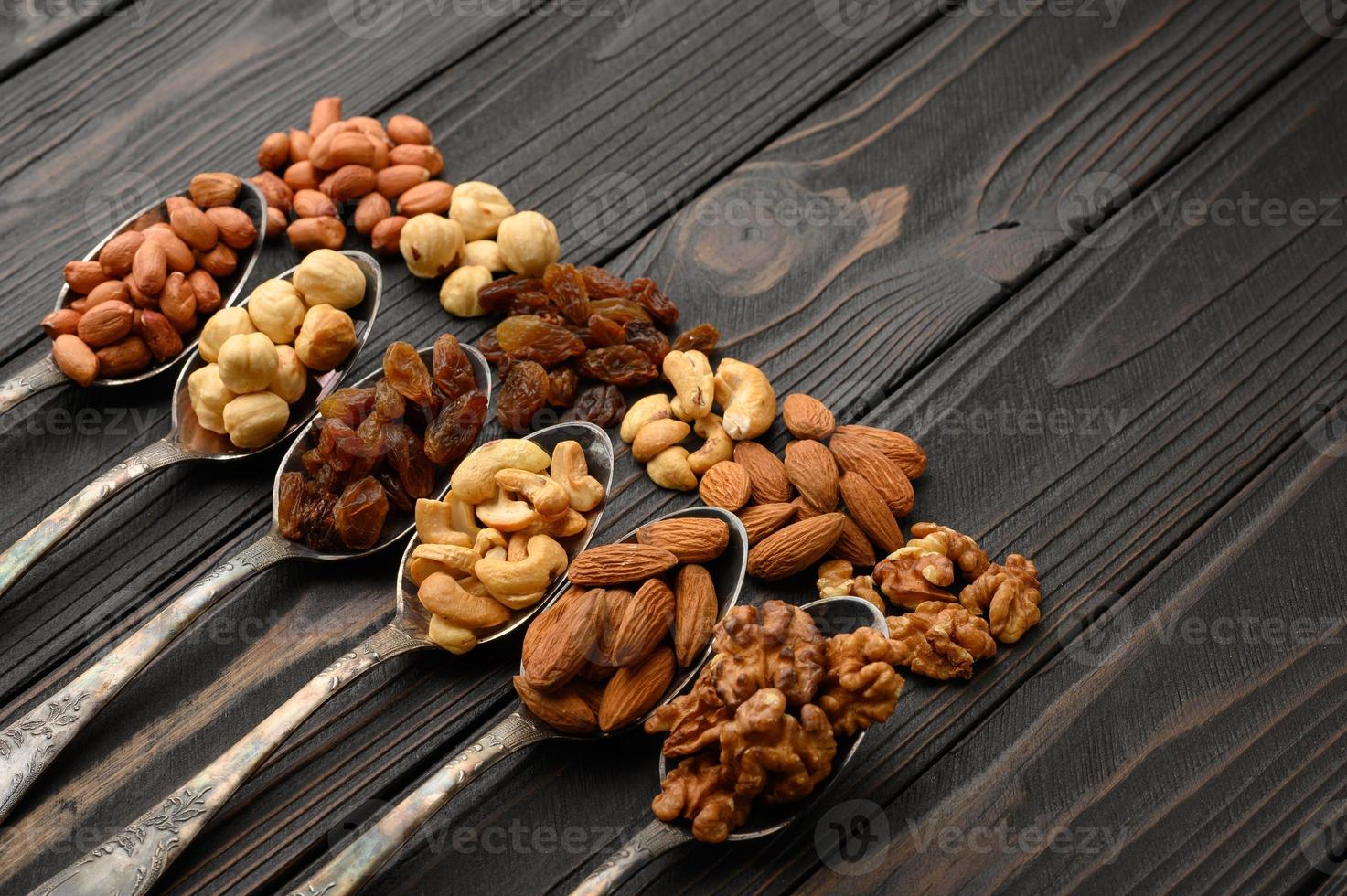 Hazelnut, cashews, raisins, almonds, peanuts, walnuts in silver spoons on a rustic background photo