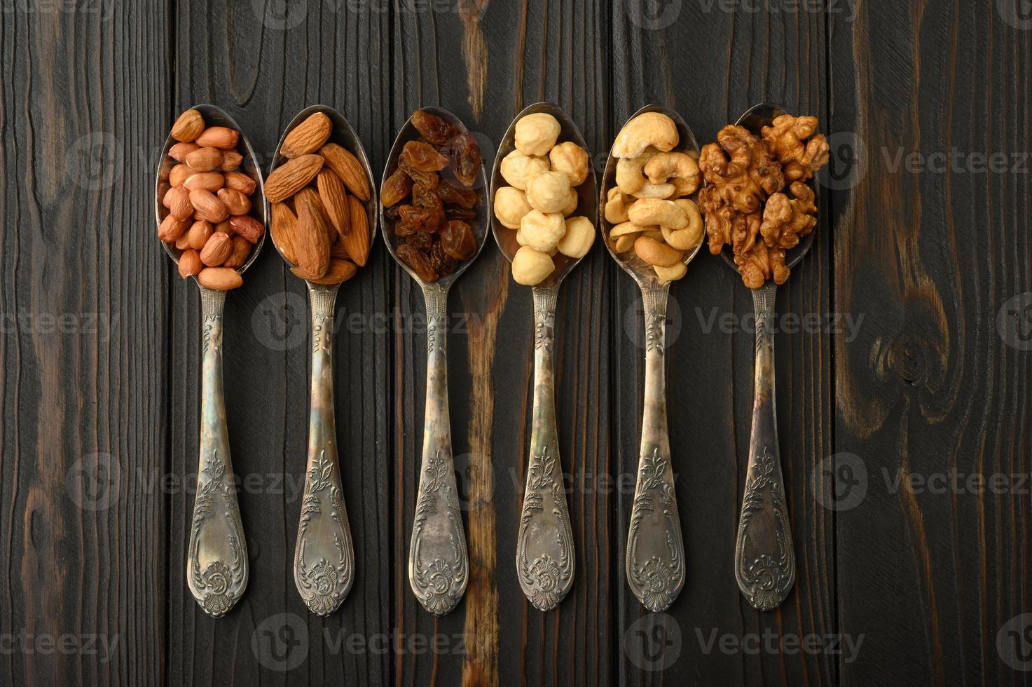 Hazelnut, cashews, raisins, almonds, peanuts, walnuts in silver spoons on a rustic background photo