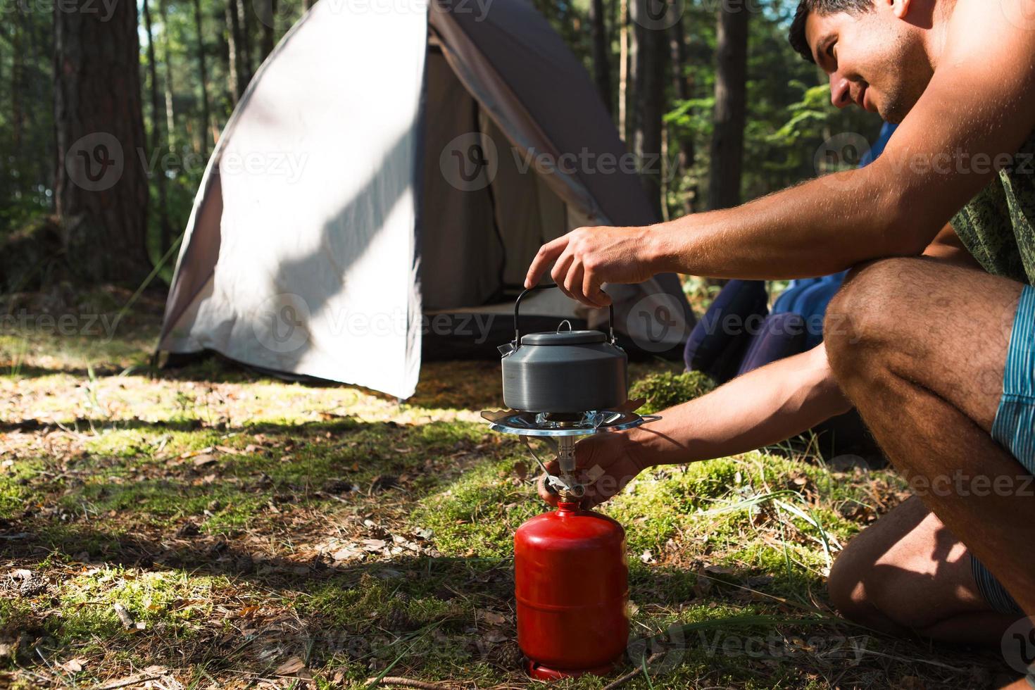 Cooking, heating a tourist kettle on a portable gas burner with a red gas cylinder. Camping, a man cooks breakfast outdoors. Summer outdoor activities photo