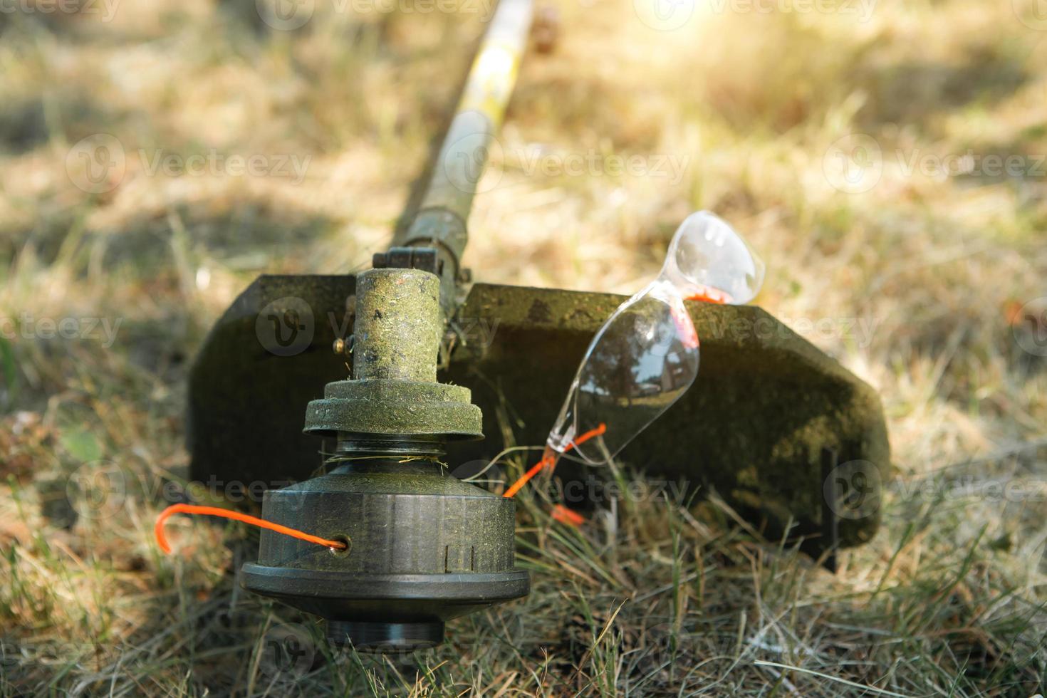 recortadora después de cortar la hierba de cerca. bomba de gasolina en el césped con gafas de seguridad. paisajismo y paisajismo de la parcela del jardín, cuidado del césped. foto