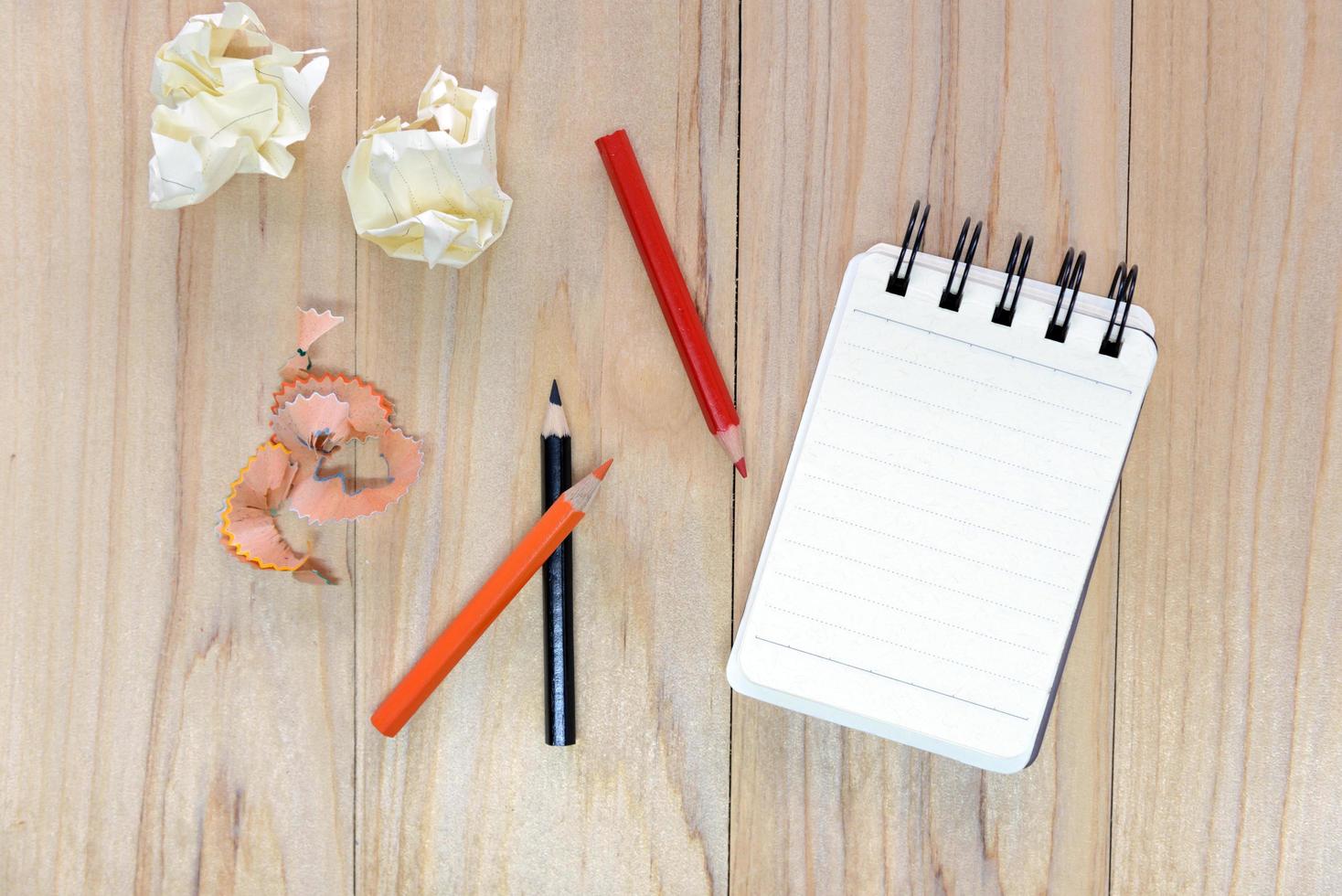 Small note book paper or notepad for writing information with color pencil and crumpled paper balls on wooden table. view from above photo