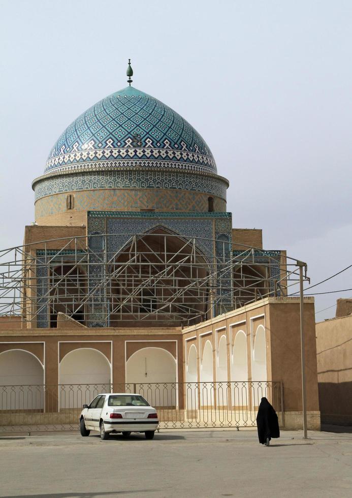 teherán, irán - 14 de junio de 2018 - una mujer con hiyab cruza una plaza junto a una mezquita en teherán, irán foto