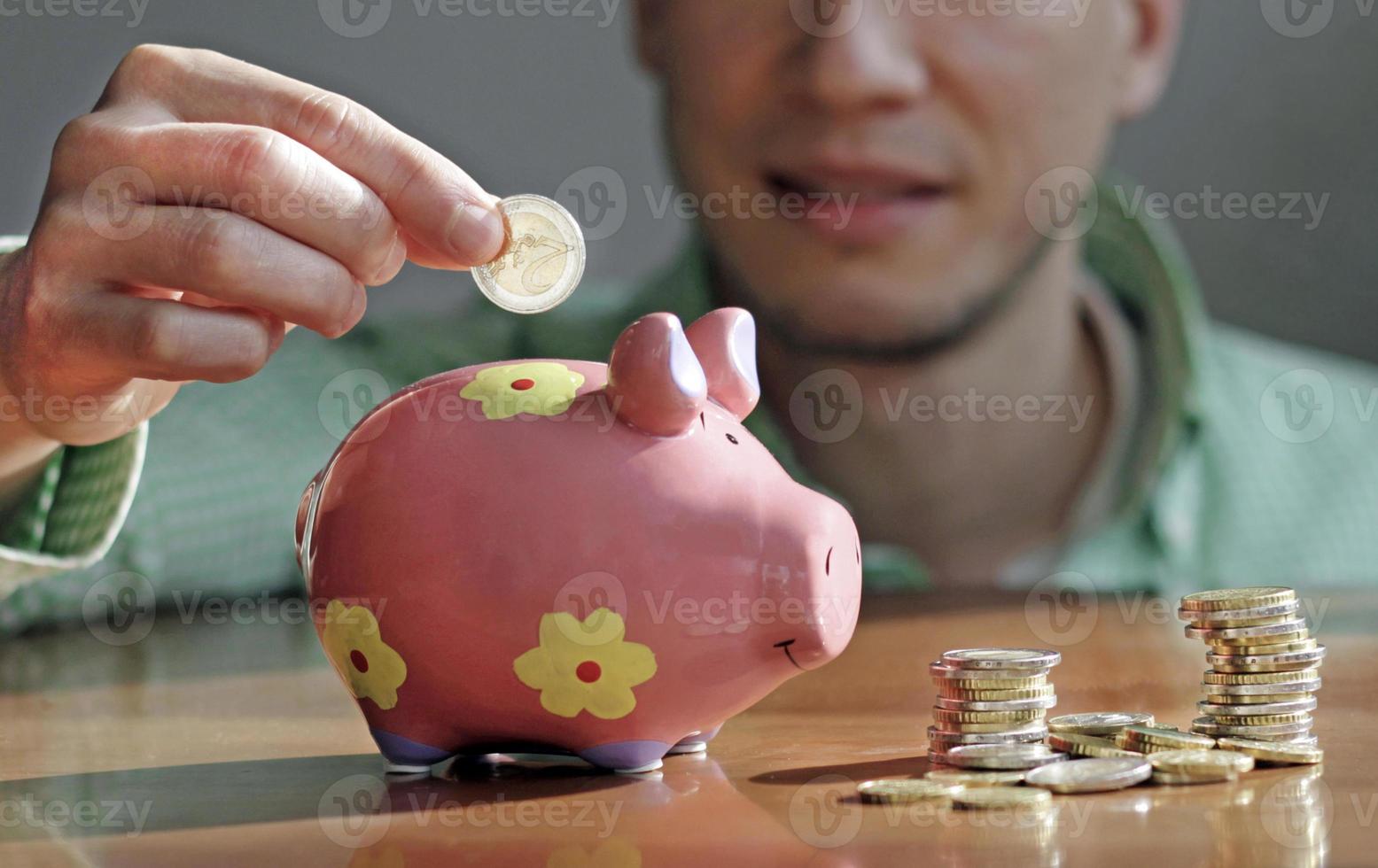 Young man putting coin in piggy bank photo