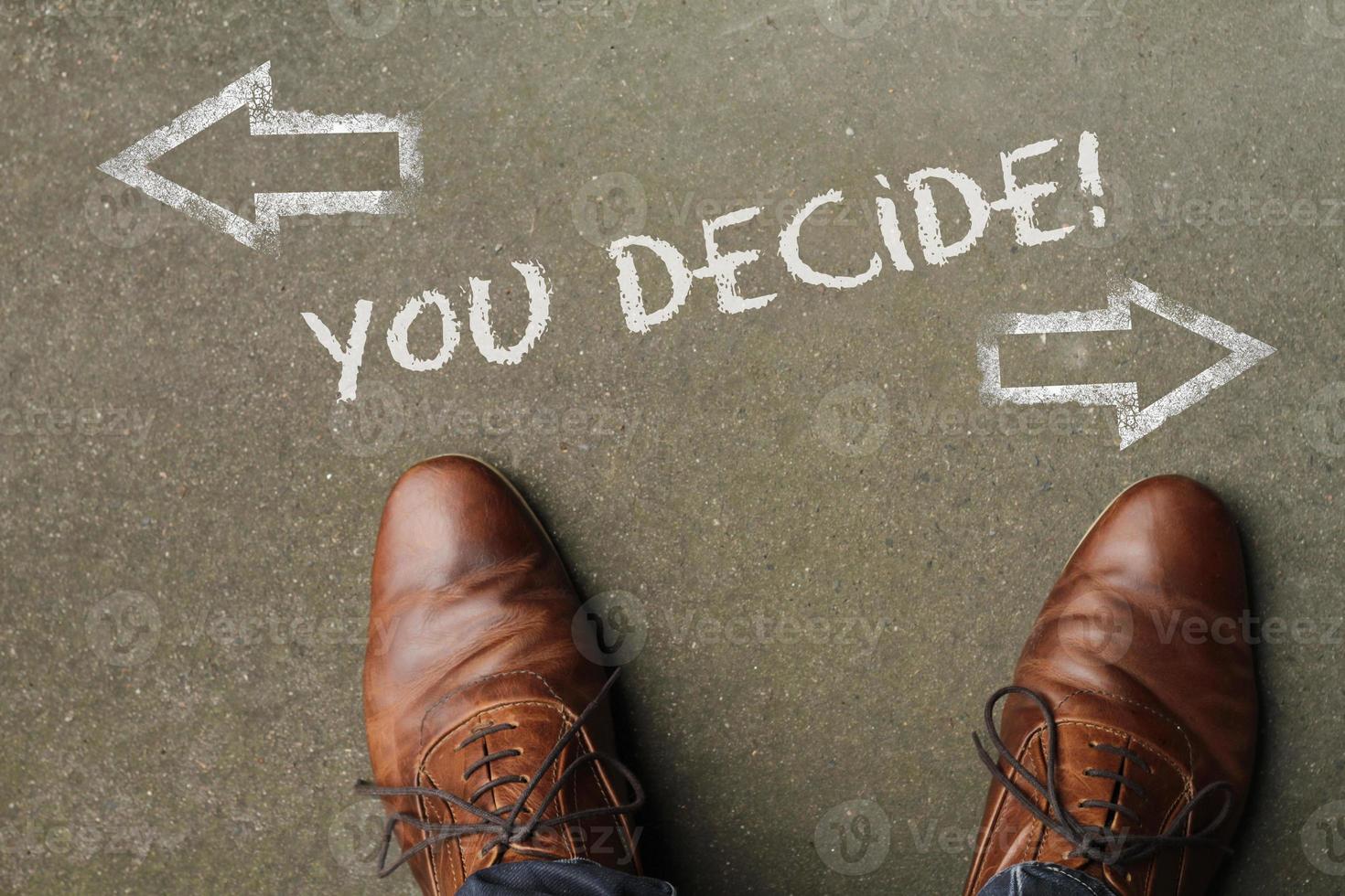 A man deciding on his future - looking down at the words You Decide written on the floor with arrows pointing in opposite directions photo