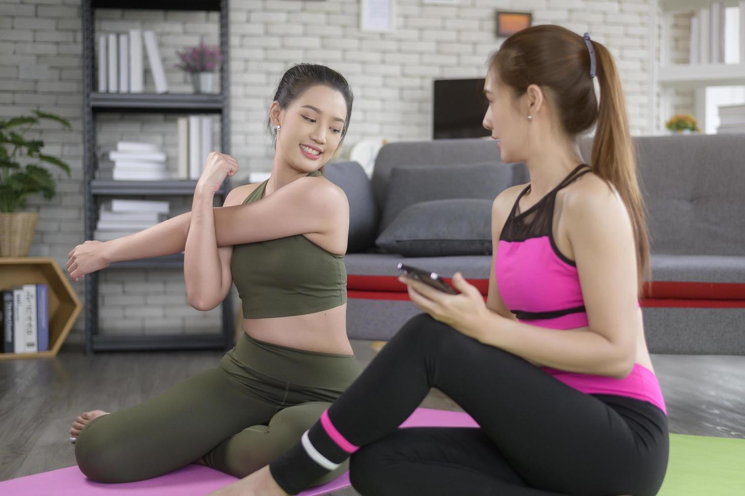 Young friend women practicing yoga at home unsing smart phone via online class with professional instructor, sport and healthy lifestyle concept. photo