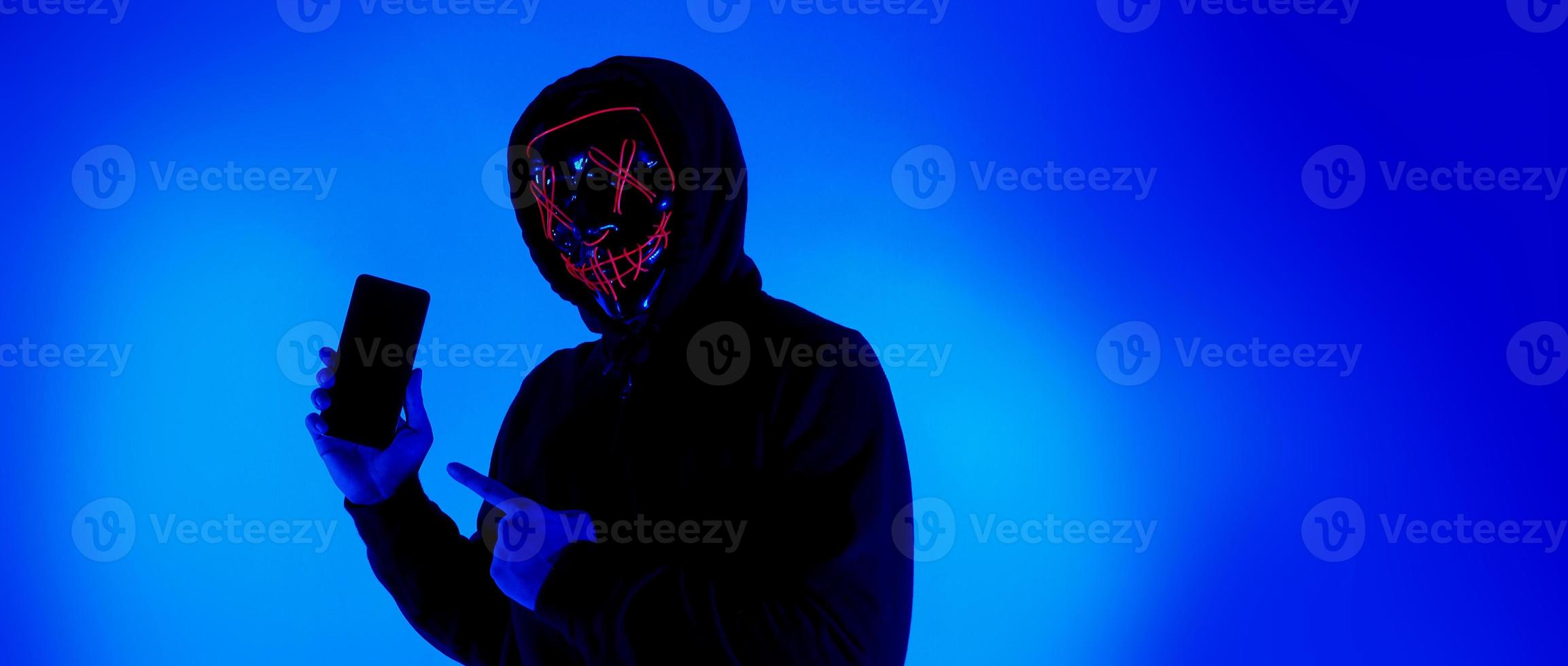 Anonymous hacker and face mask with smartphone in hand. photo