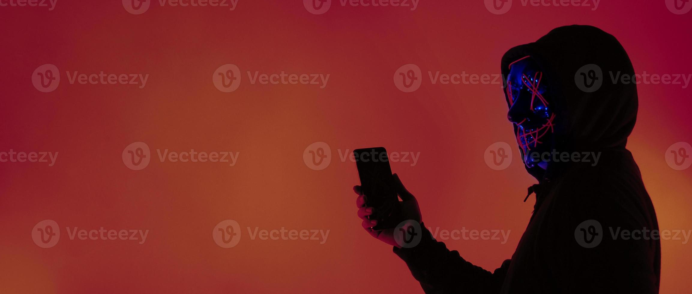 Anonymous hacker and face mask with smartphone in hand. photo