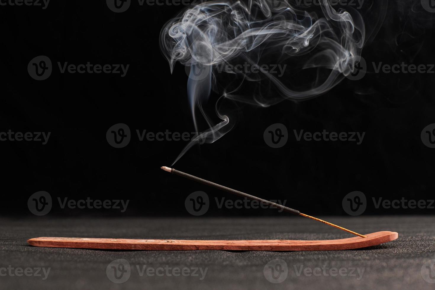 Smoke curls of burning incense stick in wooden holder for relaxation and meditation black background photo