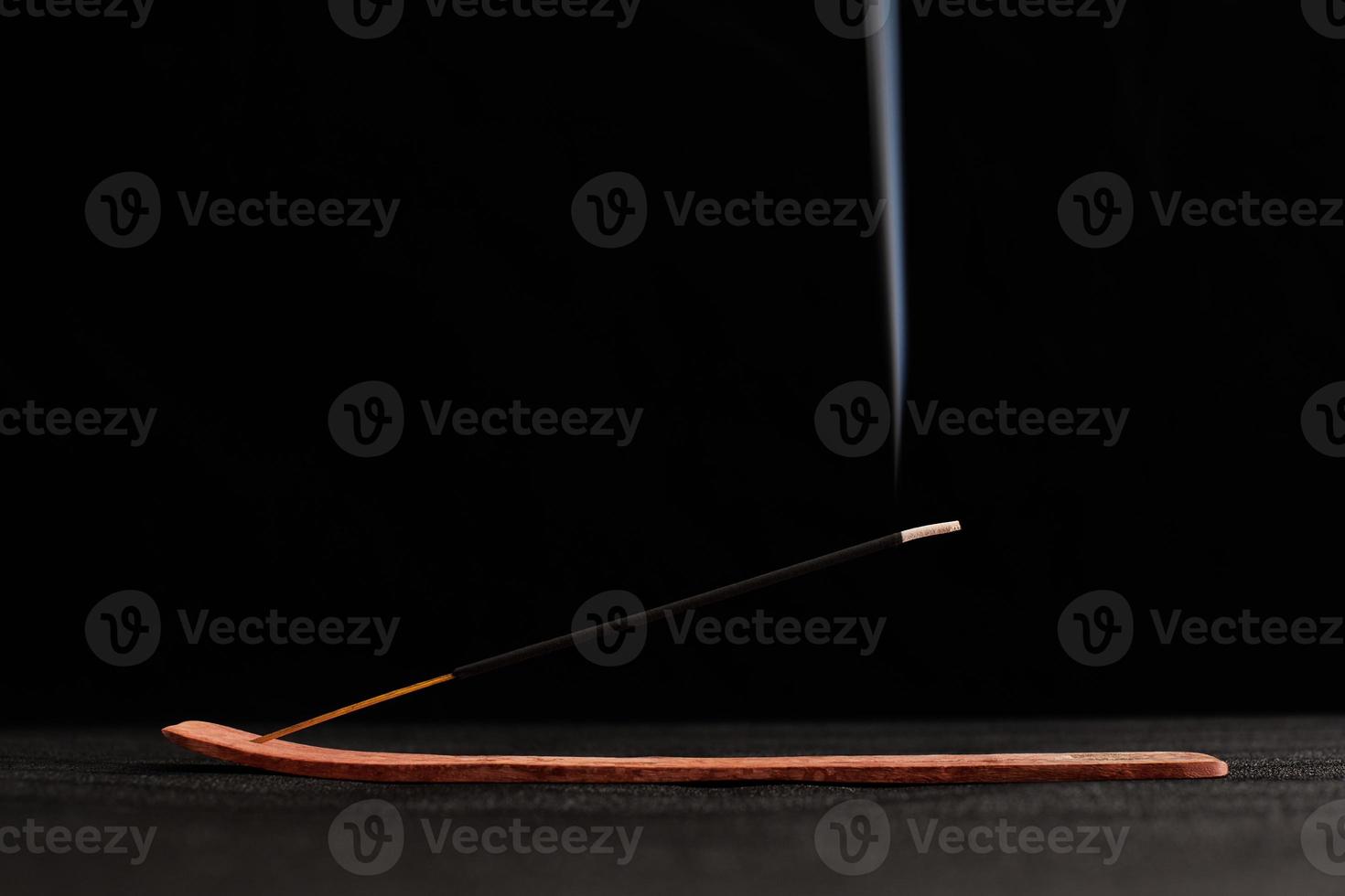 Smoke curls of burning incense stick in wooden holder for relaxation and meditation black background photo