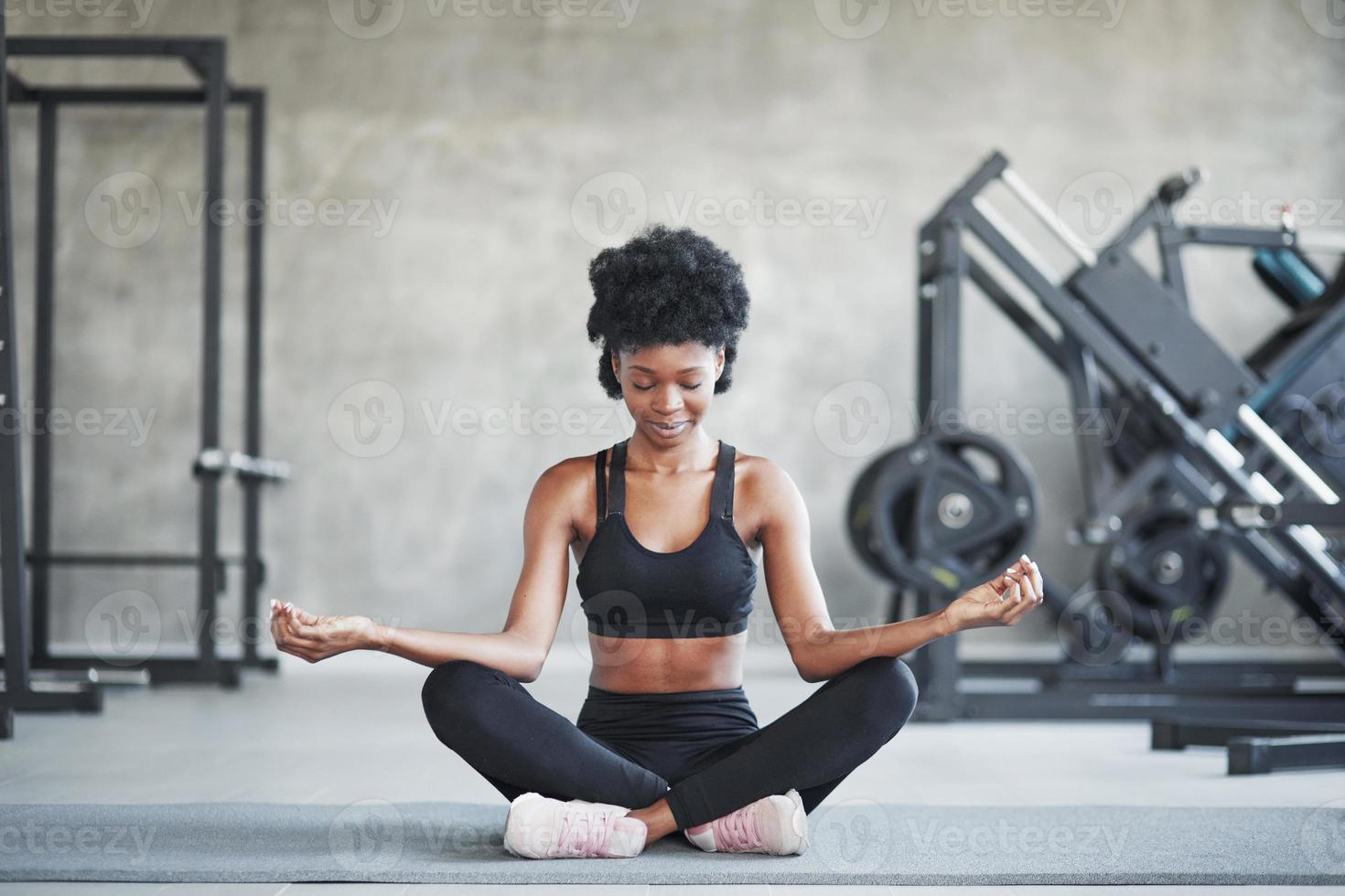 Meditation and relaxation. African american woman with curly hair and in sportive clothes have fitness day in the gym photo