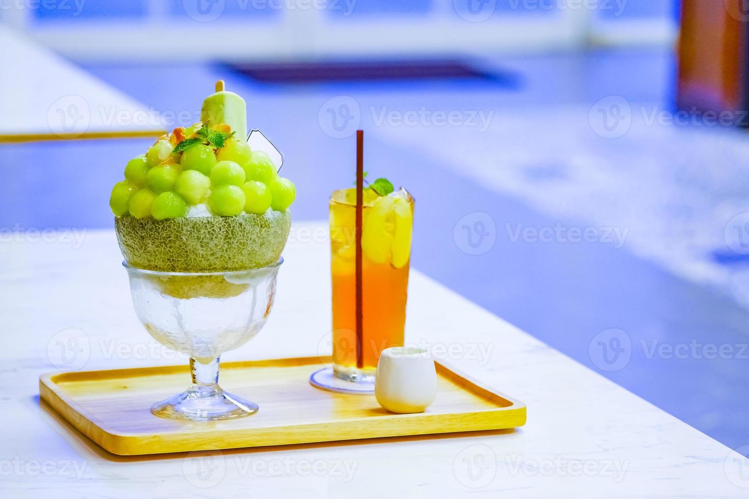 green melon ball shape are arranged on the top of bingsu korean icecream style and decorated with green tea ice-cream and mint leaf on the wood plate and Sweetened condensed milk beside. photo
