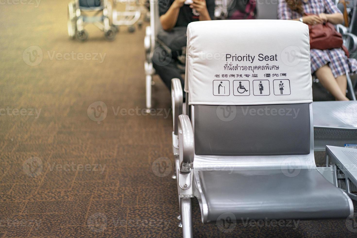 White and grey piority seat near gateway in the airport, with blur passengers behind. Thai and Chinese language  means piority seat photo