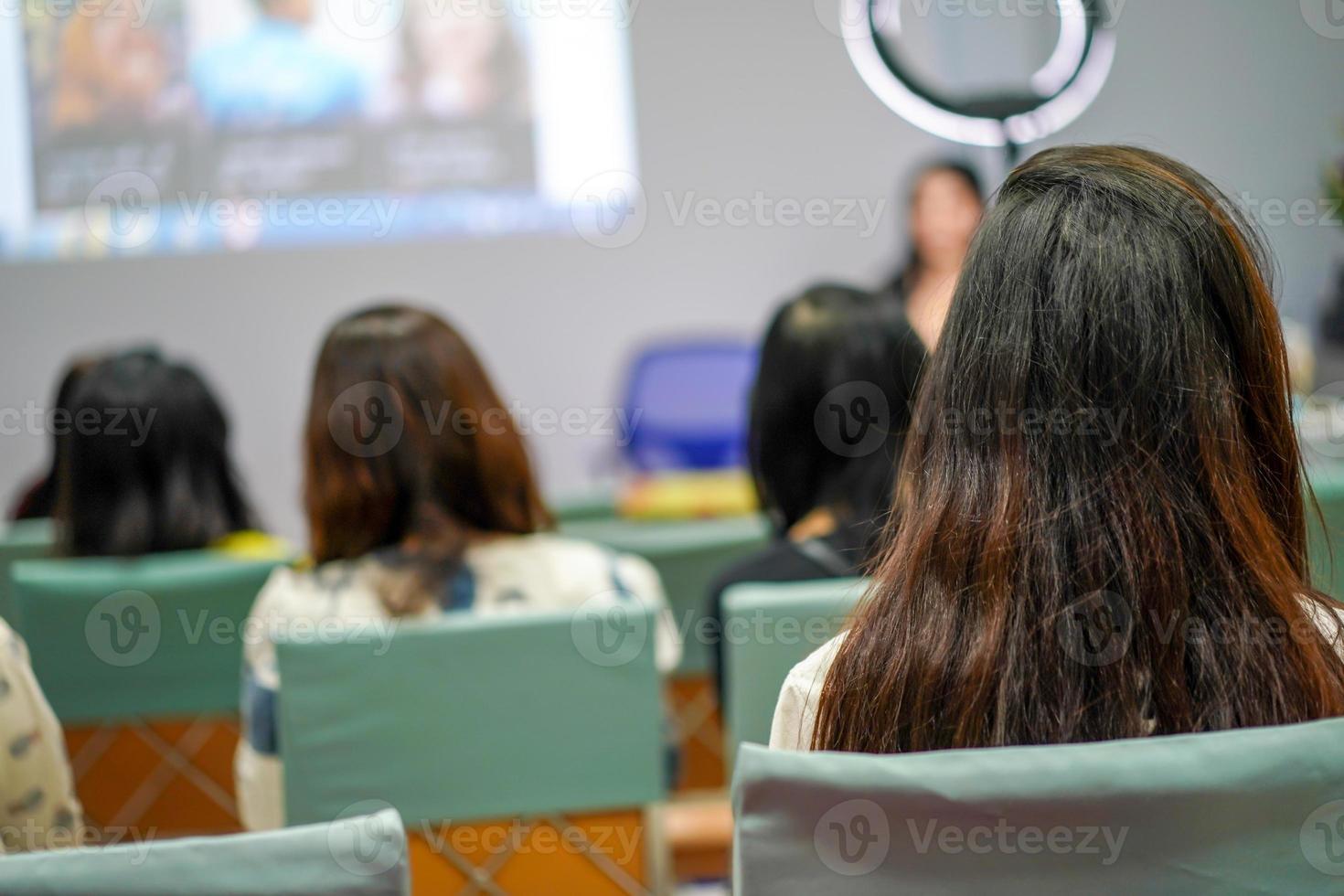la audiencia y los participantes escuchan al profesor y al disertante al frente del escenario sobre el maquillaje facial de las mujeres. foto