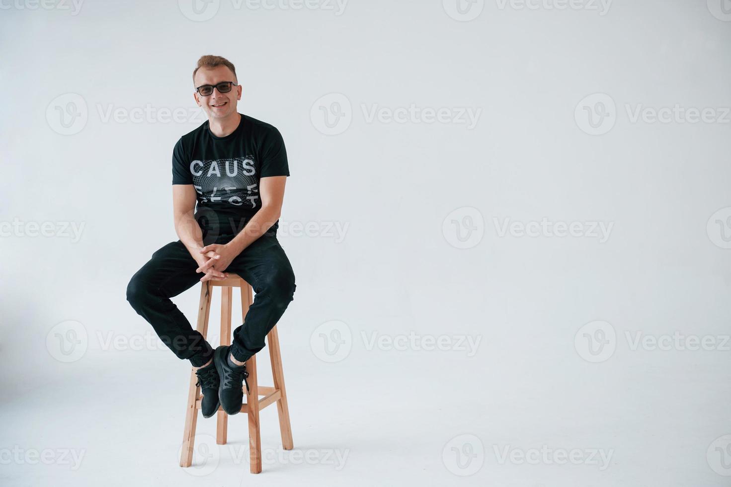 Smiling to the camera. Positive man in casual clothes have fun in the studio against white wall photo