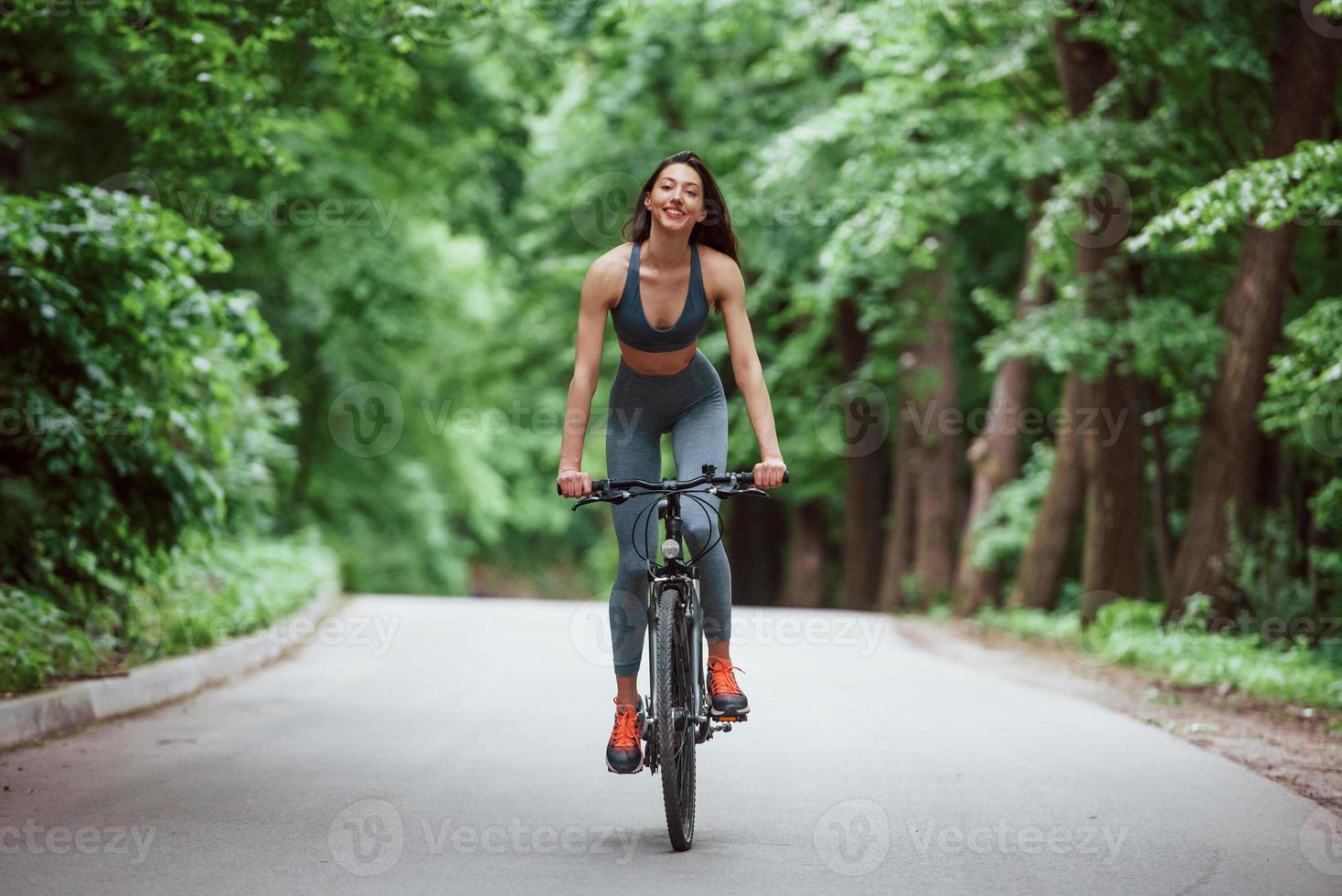 Female cyclist on a bike on asphalt road in the forest at daytime photo