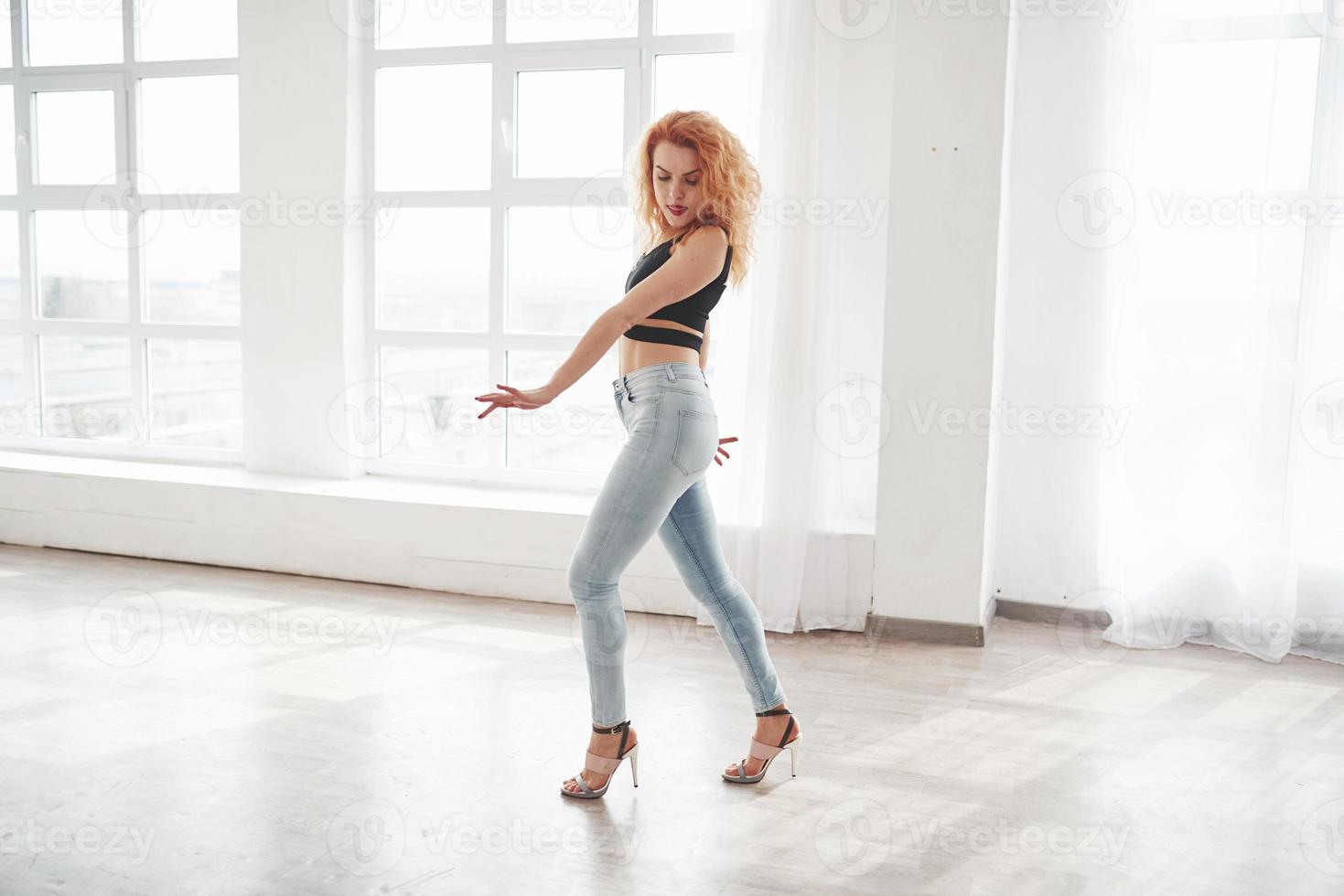 Showing nice dance moves. Attractive redhead woman posing in the spacey room near the window photo