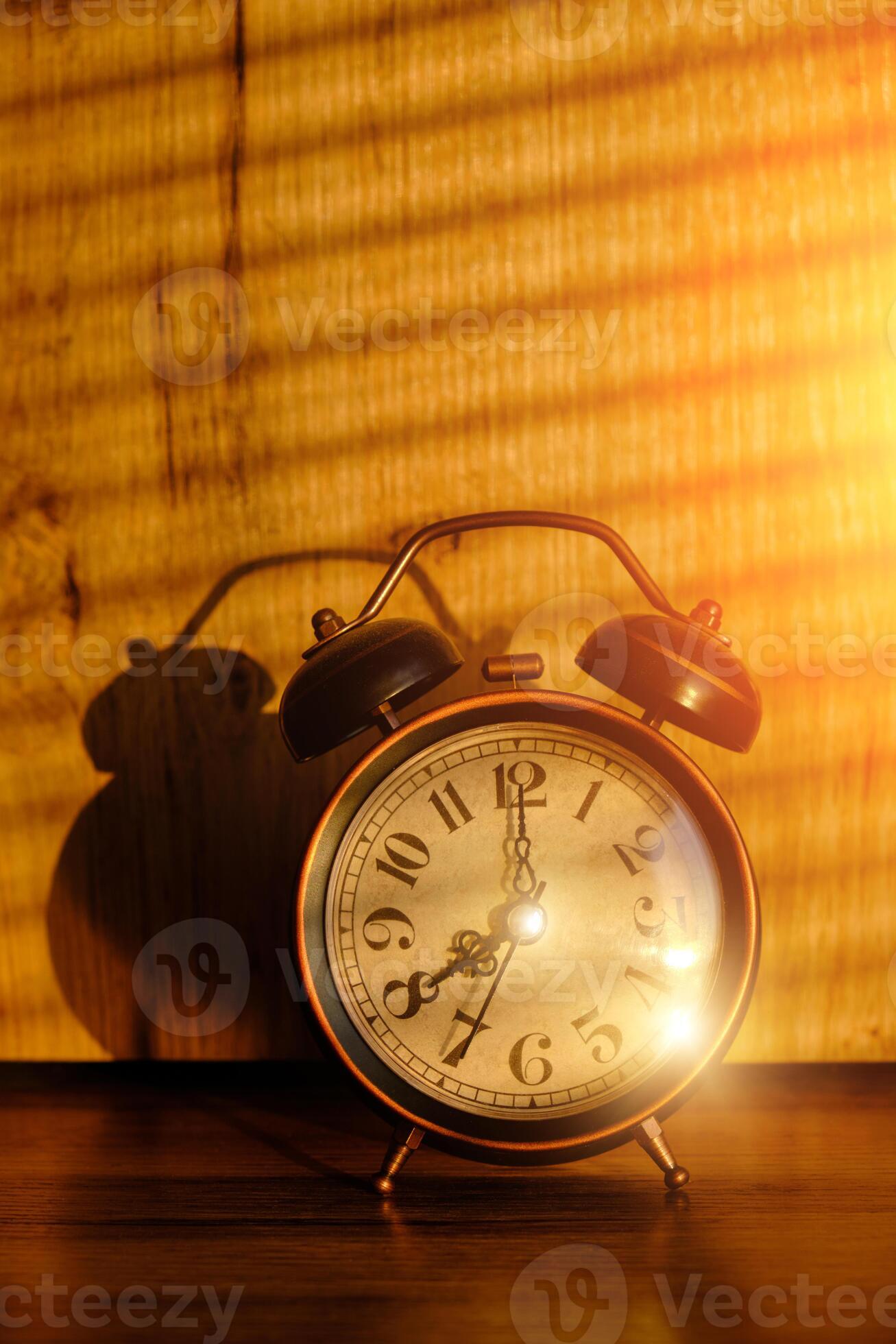 Old retro alarm clock in early morning on table, shadows from blinds on