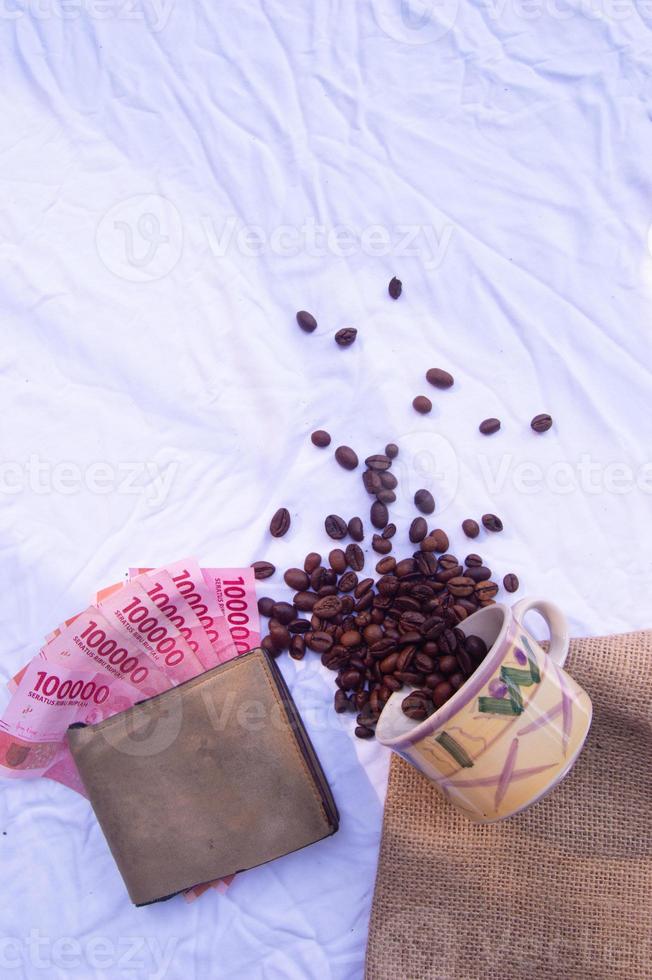 Photo of coffee beans in a spilled glass and rupiah notes with a wallet and white background