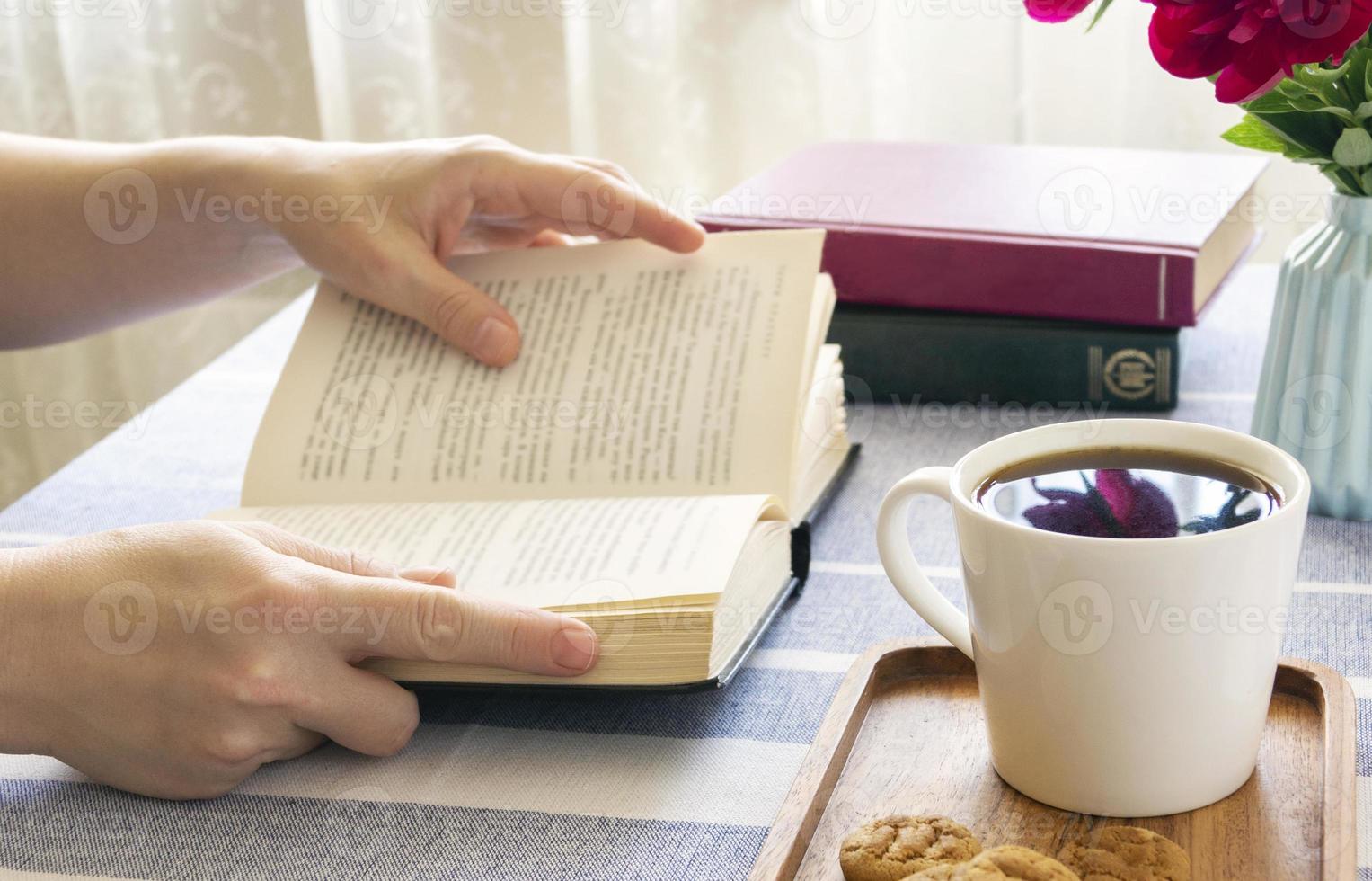 Reading a book at a table by the window. Book in hand,morning coffee at home or in a cafe, cozy atmosphere. photo