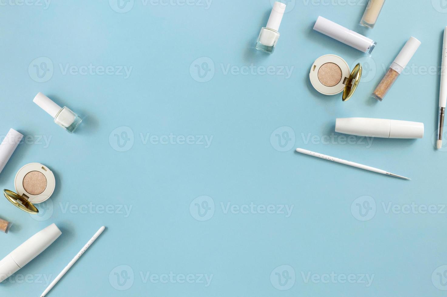 White makeup cosmetics on a blue background with copy space. On the table are shadows, mascara, brushes, lipstick, top view. photo