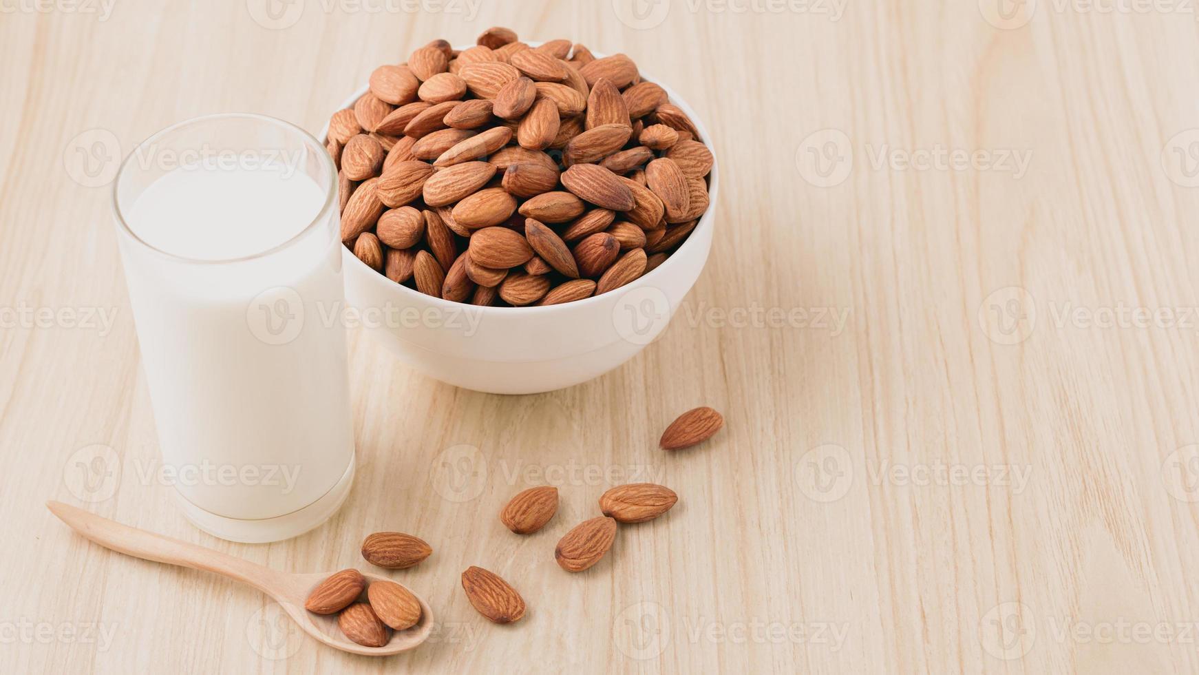 Almond nuts in a white bowl and milk in glass on wood background with nuts in spoon around the bowl.selective focus.front view. copy space. photo