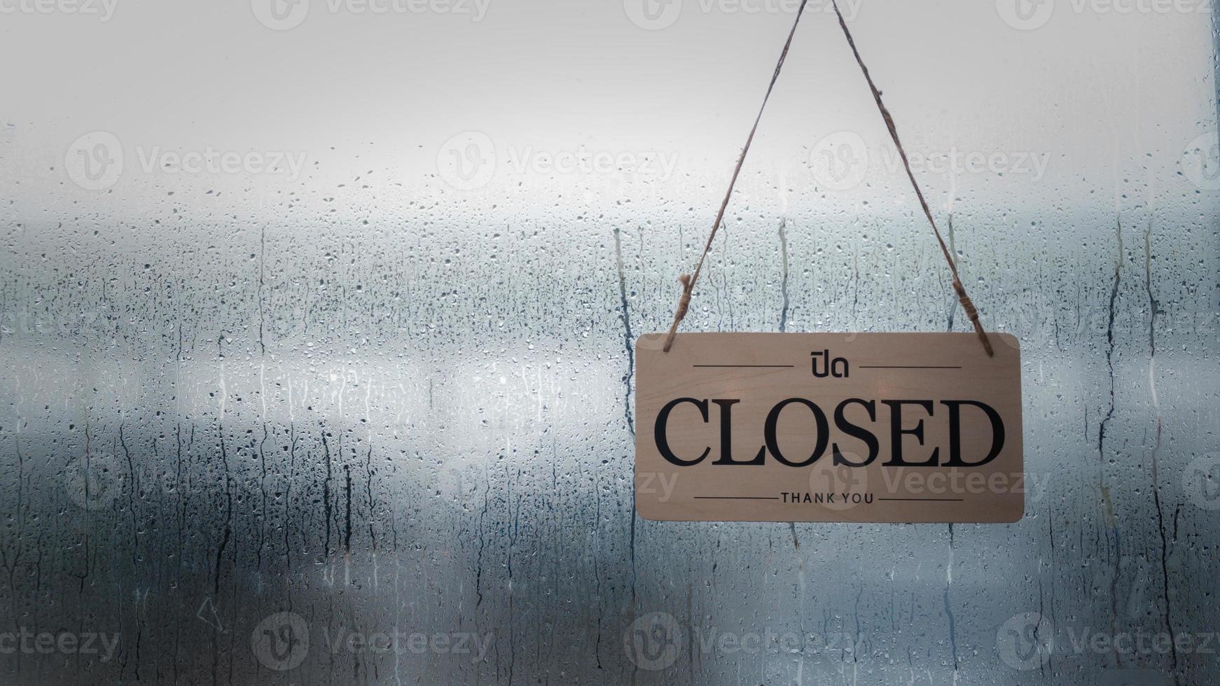 A closed sign hanging in front of a shop window on a rainy day.copy space. photo