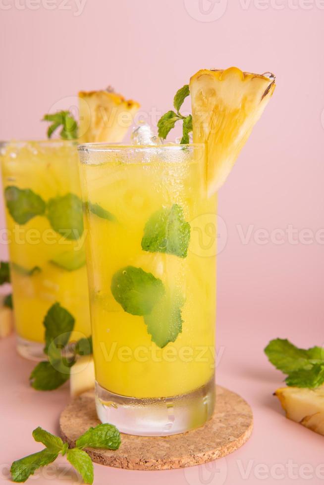 Pineapple cocktail or fresh pineapple juice, mint leaves in glass with ice and  pineapples on a pink background. selective focus. photo
