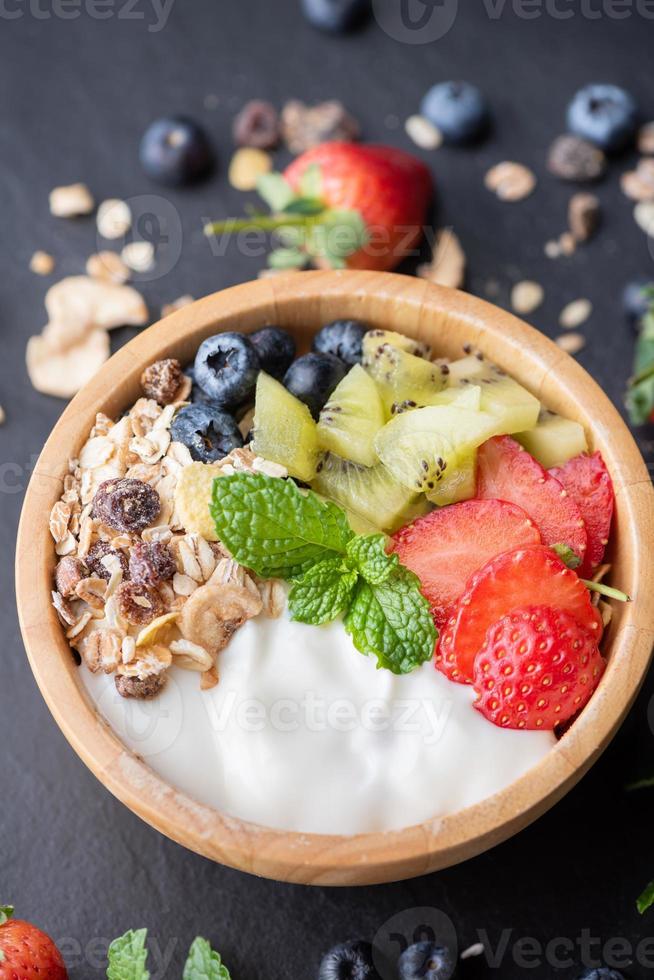 bowl of oat granola with yogurt, fresh blueberries, strawberries, kiwi mint and nuts board for healthy breakfast,  Healthy breakfast menu concept. On the black rock photo