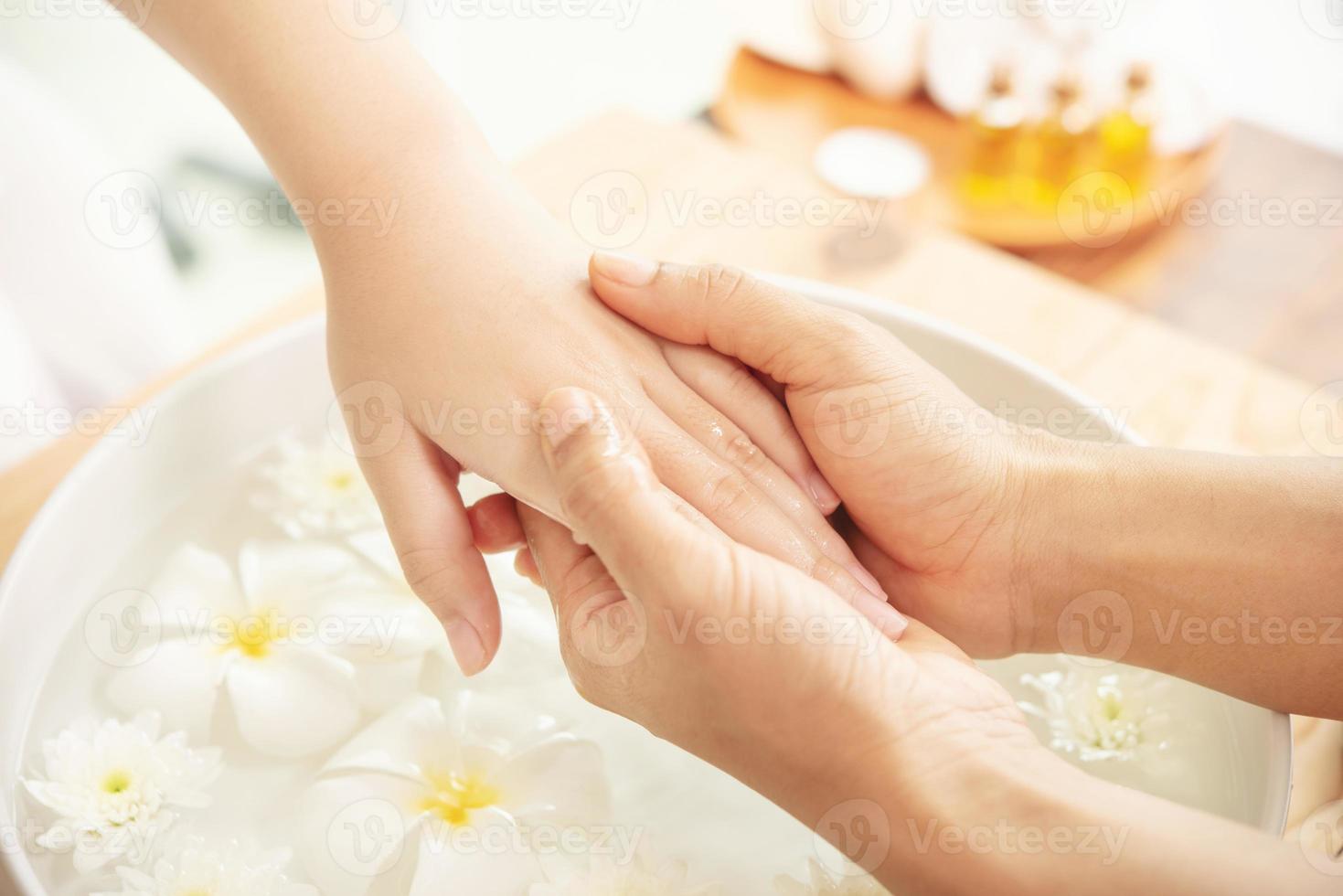 Beautician massaging hand of female spa salon client. Spa treatment and product for female feet and hand spa. white flowers in ceramic bowl with water for aromatherapy at spa. photo