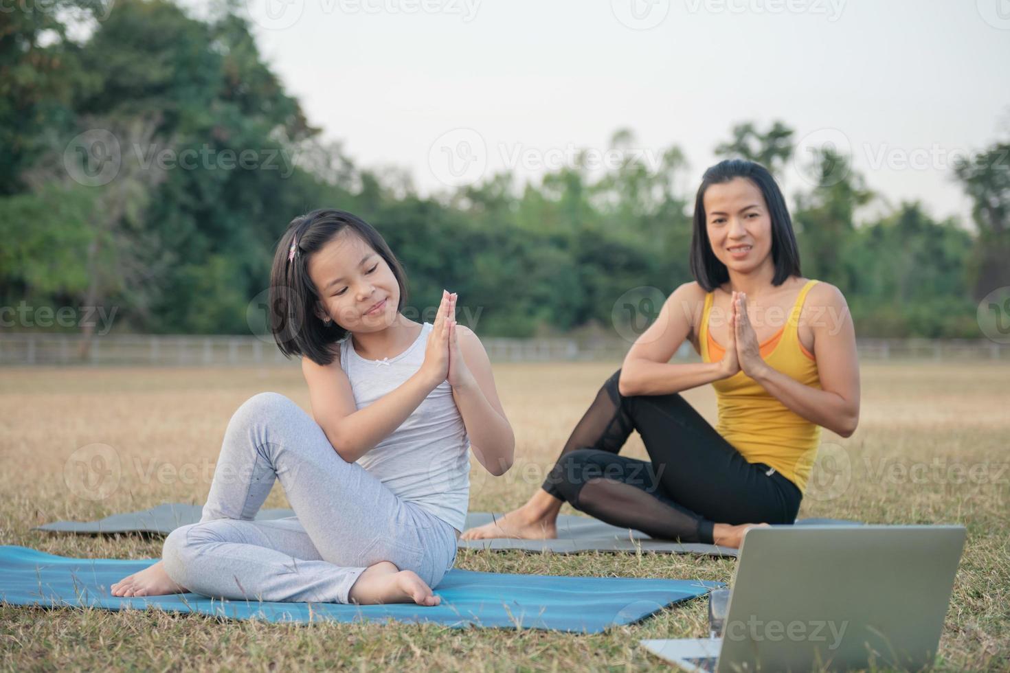 Mother and daughter doing yoga. woman and child training in park. outdoor sports. healthy sport lifestyle, watching yoga exercises online video tutorial and stretching in  Ardha Matsyendrasana pose photo