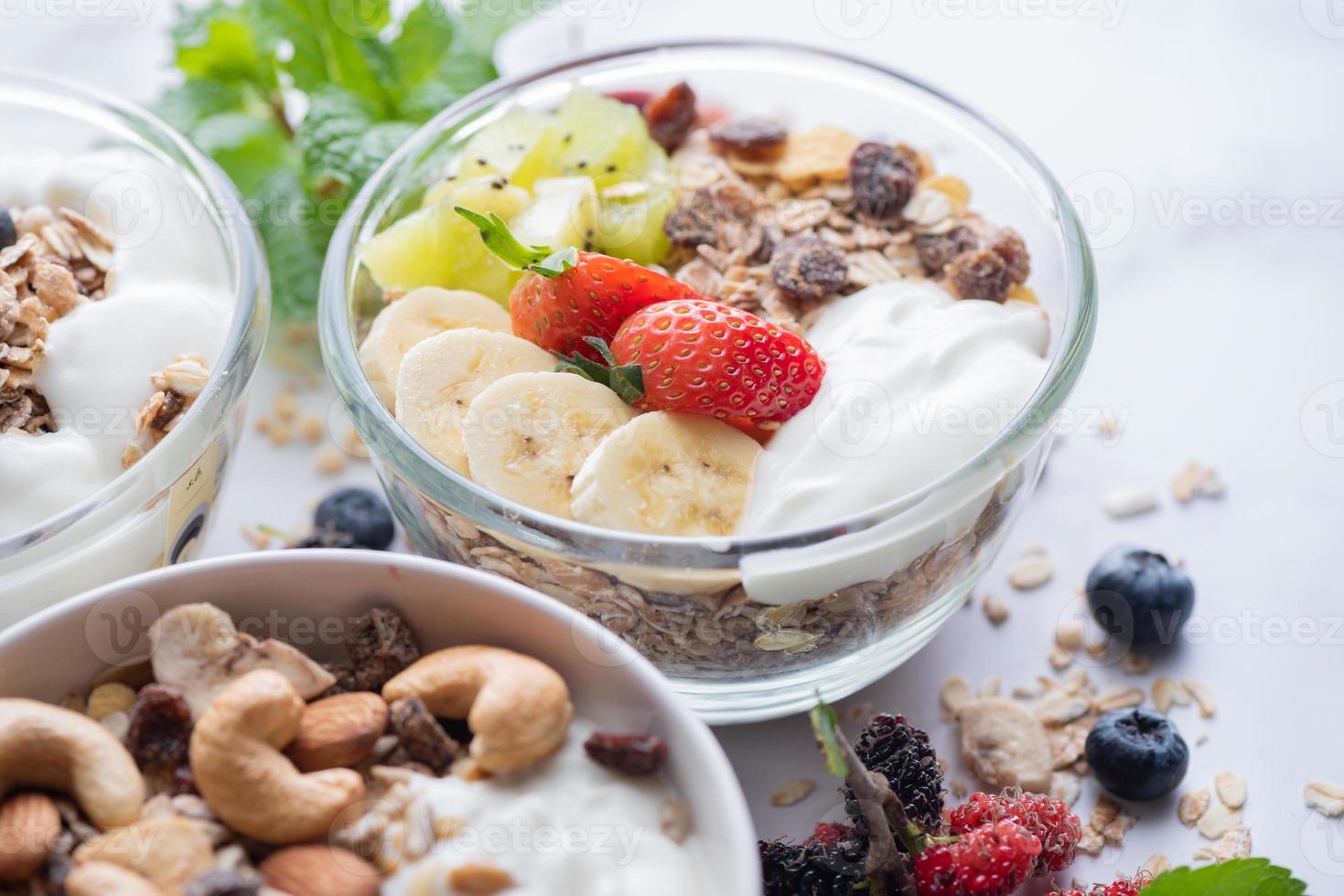 bowl of oat granola with yogurt, fresh blueberries, mulberry, strawberries, kiwi, banana, mint and nuts board for healthy breakfast, top view, copy space, flat lay. vegetarian food concept. photo