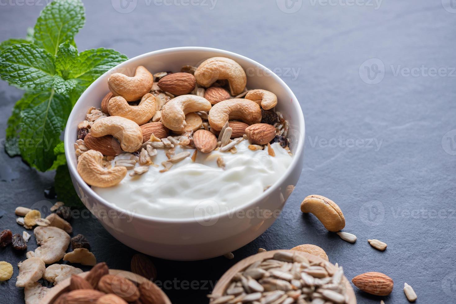 Homemade granola or muesli, bowl of oat granola with yogurt, almond, Cashew nuts, mint and nuts on the black rock board for healthy breakfast, copy space. Healthy breakfast menu concept. photo