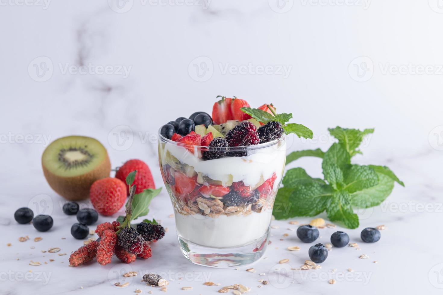 Homemade muesli, bowl of oat granola with yogurt, fresh blueberries, mulberry, strawberries, kiwi, mint and nuts board for healthy breakfast, copy space. Healthy breakfast concept. Clean eating. photo