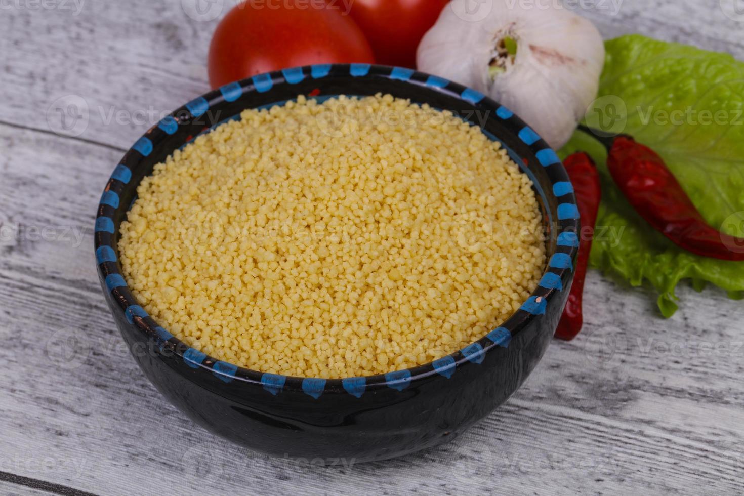 Raw couscous in the bowl served salad leaves, tomato and pepper photo