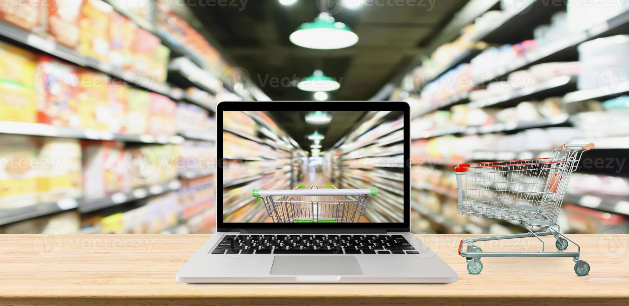 supermarket aisle blurred background with laptop computer and cart on wood table online shopping concept photo