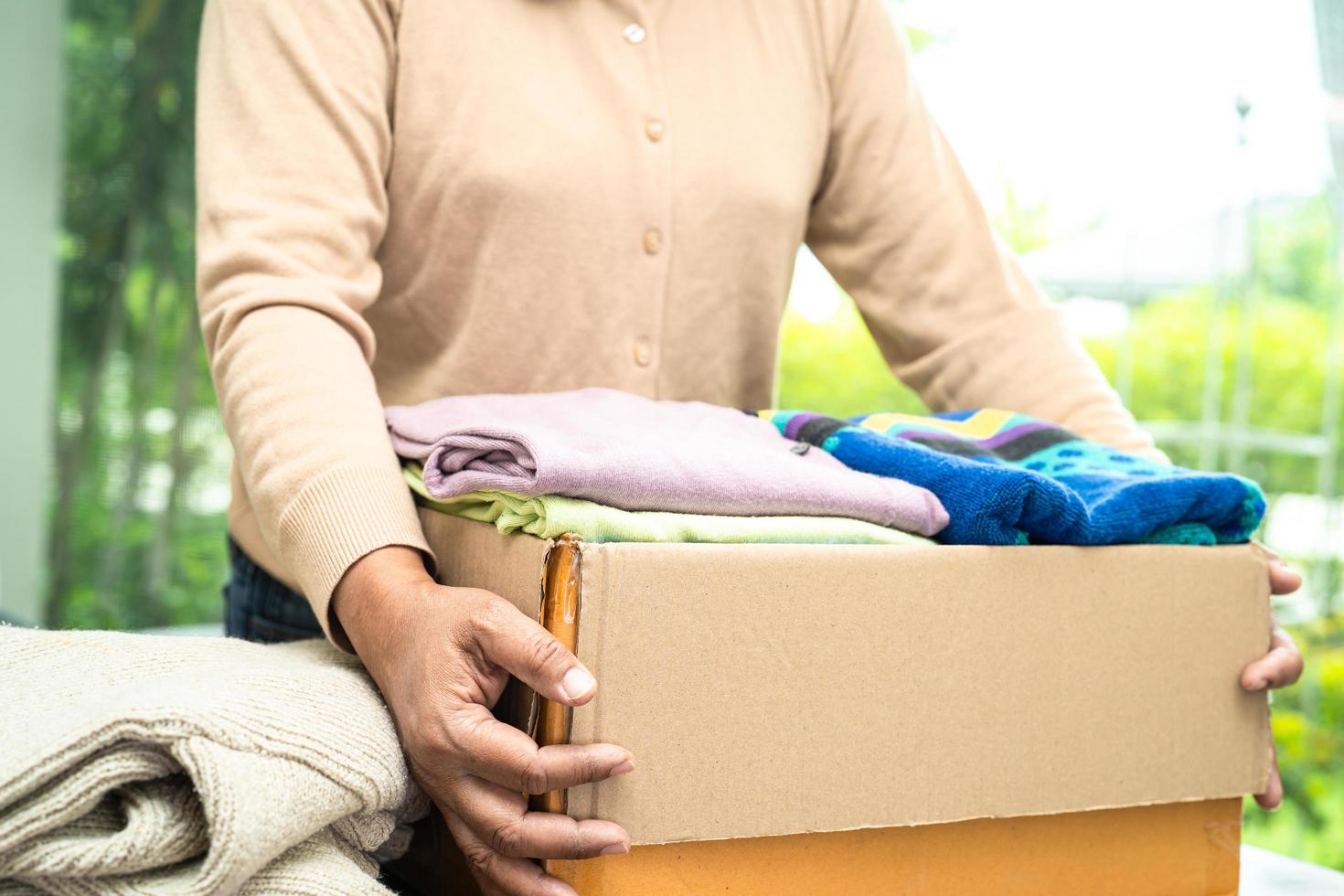 sosteniendo una caja de donación de ropa con ropa usada y muñecas en casa para apoyar la ayuda a los pobres del mundo. foto