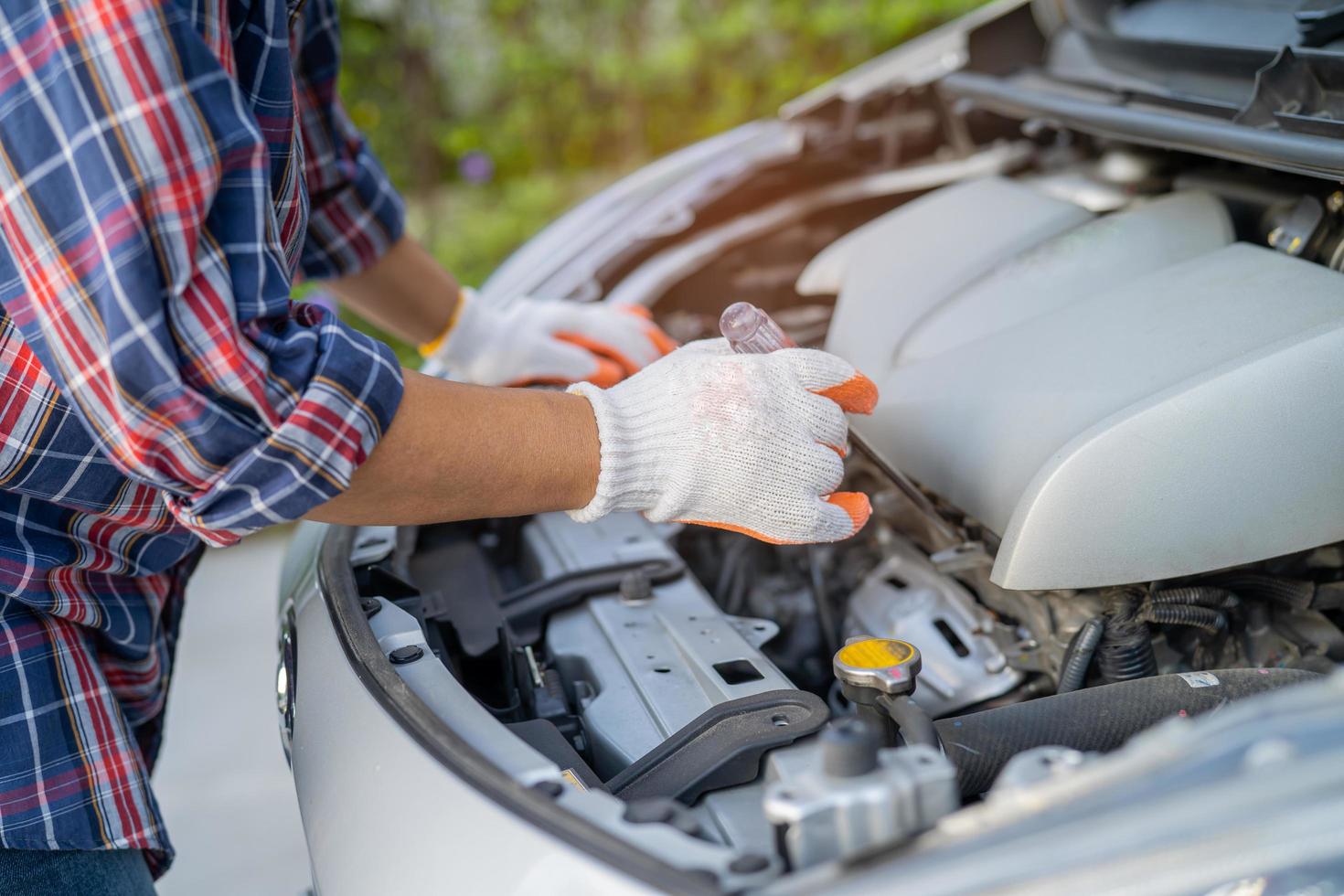 Asian auto mechanic check for repair under the hood of broken down car on the side of the road. photo