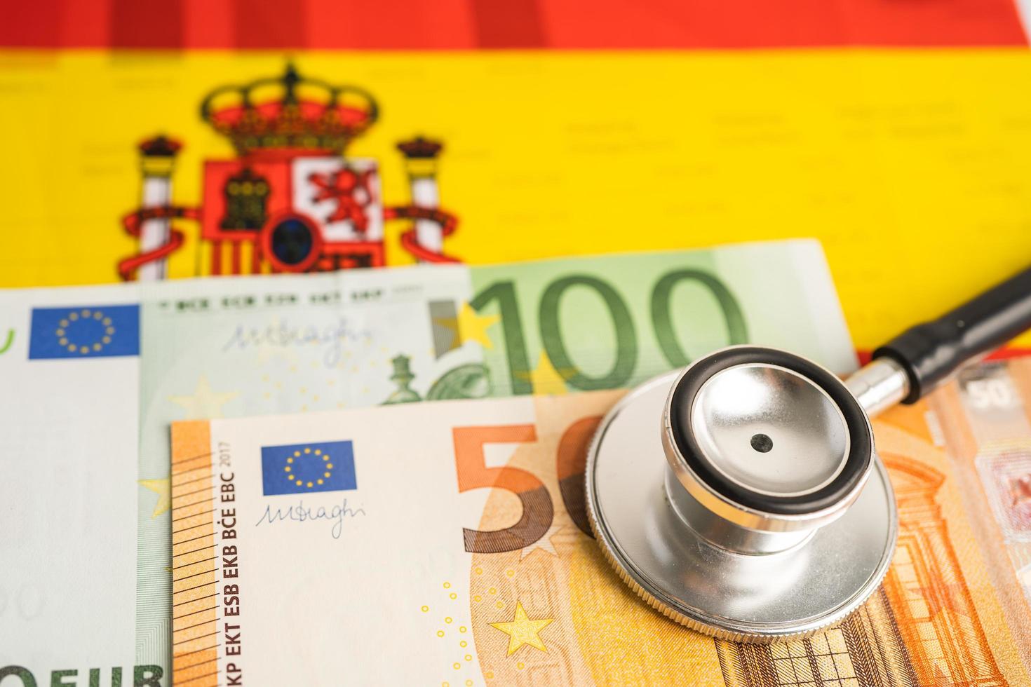 estetoscopio negro con billetes en euros sobre fondo de bandera española, concepto de negocios y finanzas. foto