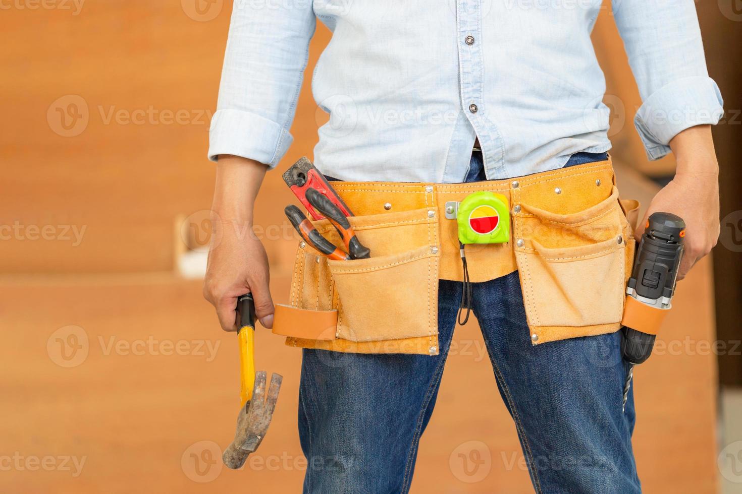 Handyman manual worker in tools belt and holding drill in his hands, Carpenter working with equipment in wood workshop, man doing woodwork in carpentry shop photo