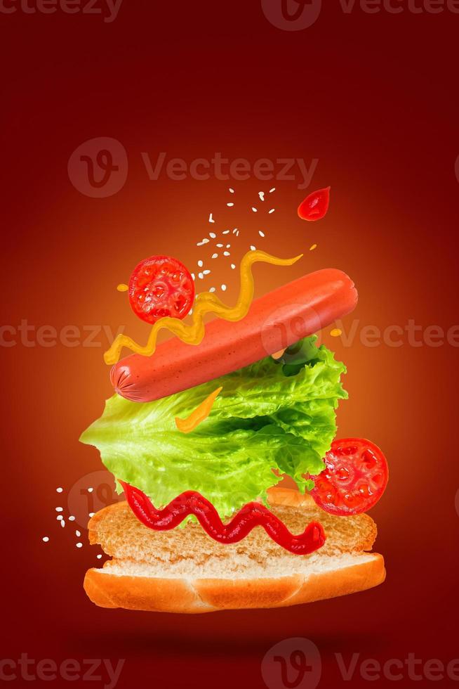 Flying ingredients for delicious hot dog on red background. Levitating sausage, tomatoes and lettuce. photo