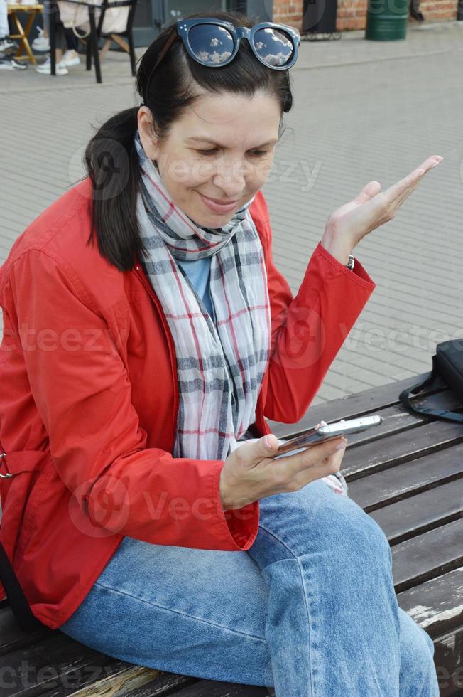 Photo of a satisfied smiling woman holding a mobile phone and moving her hand to the side. A girl, a young woman is surprised to read a message in a smartphone.