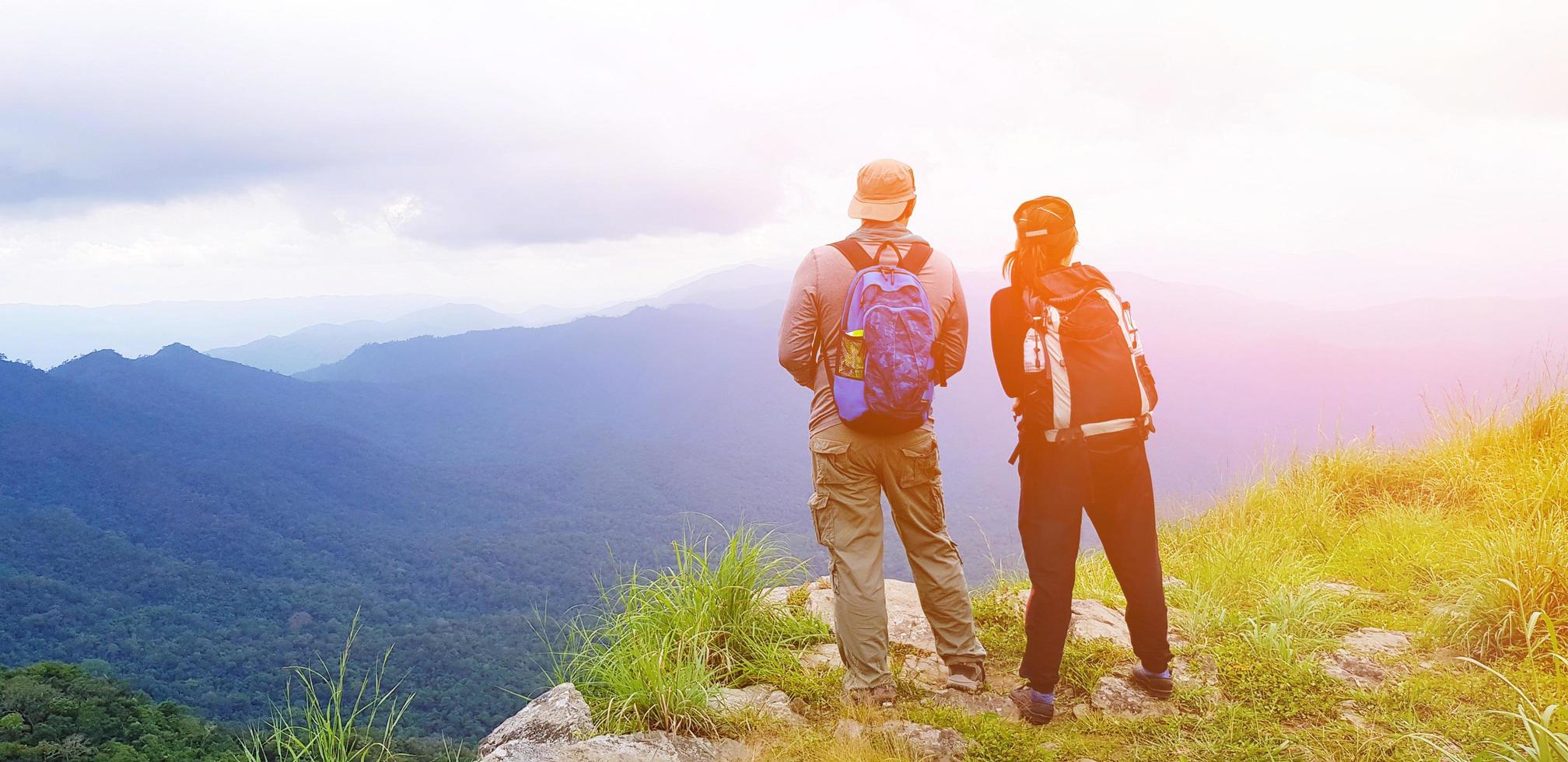 Couple hiker with backpack standing on the top of mountain with sunlight flare, blue sky, white cloud and mist at Doi Luang Tak, Thailand - Landscape view, Beauty of Nature and Landmark for Tourist photo