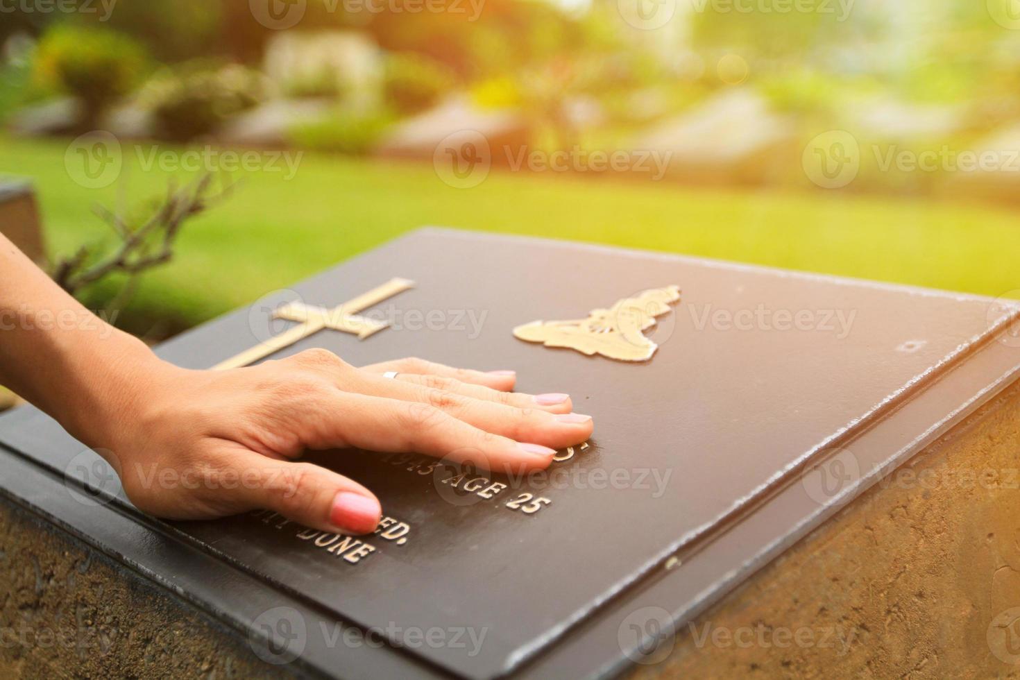 Woman's hand touching the black stone grave at cemetery with orange sunlight flare . photo